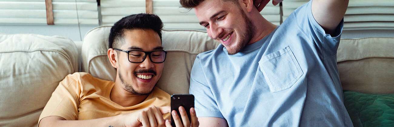 Two casually dressed young guys smile at something on a mobile phone