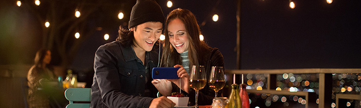 Couple at nighttime cafe smile while looking at a phone