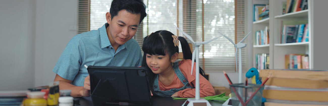 Dad and daughter on a tablet explore online together in a craft and STEM hobby room where she is building a wind turbine model